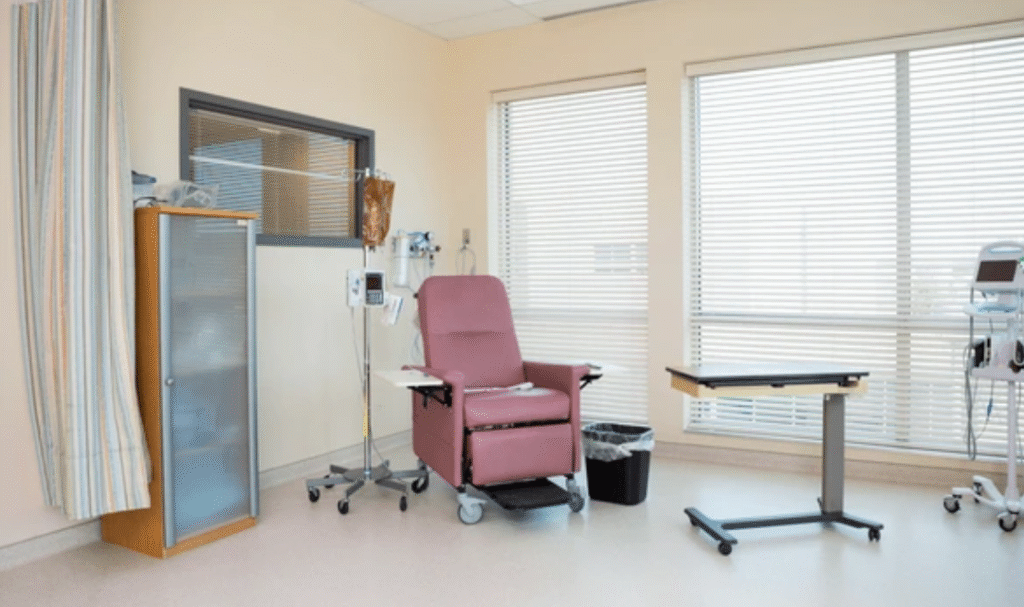 Patient care equipment in a safe hospital-style bedroom with bed rails, overbed table, trapeze, and geri chair arranged for caregiver access