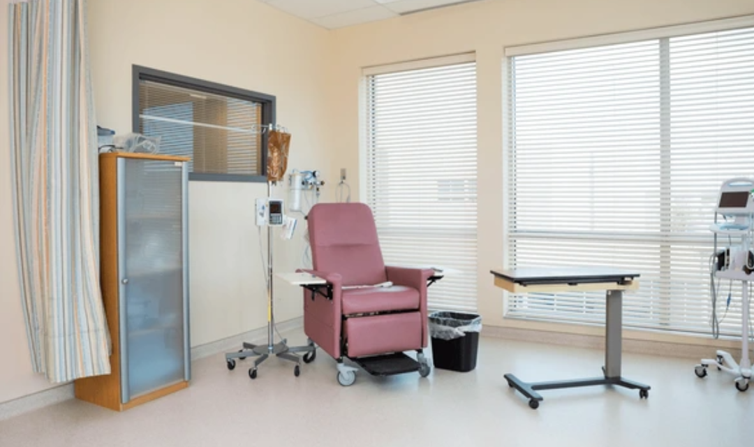 Patient care equipment in a safe hospital-style bedroom with bed rails, overbed table, trapeze, and geri chair arranged for caregiver access